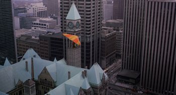 Movie still from “Short Circuit 2” (1988), directed by Kenneth Johnson – An aerial view of a clock tower in the middle of a city; Extreme Wide shot, Overhead angle