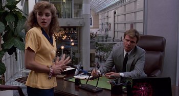 Movie still from “Short Circuit 2” (1988), directed by Kenneth Johnson – A man and a woman sitting at a table in an office setting; Medium shot, Over the shoulder angle