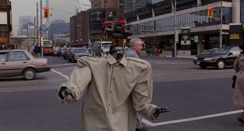 Movie still from “Short Circuit 2” (1988), directed by Kenneth Johnson – A man in a trench coat with a robot on his head walking down the street; Medium shot, Low angle