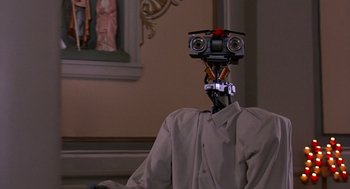 Movie still from “Short Circuit 2” (1988), directed by Kenneth Johnson – A man in a shirt and tie with a camera on his head; Close Up shot, Low angle