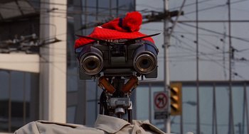 Movie still from “Short Circuit 2” (1988), directed by Kenneth Johnson – A red stuffed animal is sitting on top of a camera; Close Up shot, Low angle