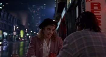 Movie still from “Short Circuit 2” (1988), directed by Kenneth Johnson – A woman sitting at a table with a man in the background; Medium shot, Over the shoulder angle