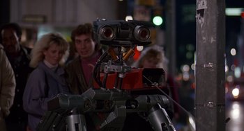 Movie still from “Short Circuit 2” (1988), directed by Kenneth Johnson – A group of people standing next to a robot; Medium shot, Low angle