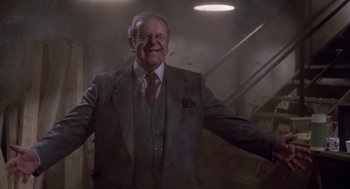 Movie still from “Short Circuit 2” (1988), directed by Kenneth Johnson – An older man in a suit and tie smiling for the camera; Medium shot, Low angle