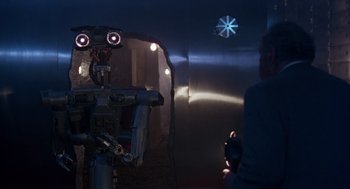 Movie still from “Short Circuit 2” (1988), directed by Kenneth Johnson – A robot is standing in front of a wall; Medium shot, Over the shoulder angle