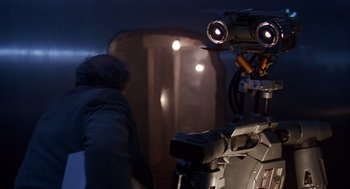 Movie still from “Short Circuit 2” (1988), directed by Kenneth Johnson – A man standing in front of a camera in front of a wall; Close Up shot, Low angle