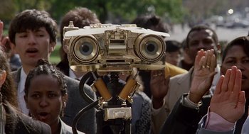 Movie still from “Short Circuit 2” (1988), directed by Kenneth Johnson – A robot head with people in the background; Close Up shot, Over the shoulder angle