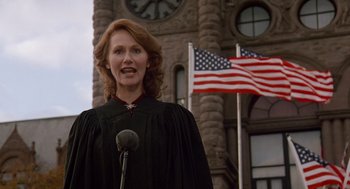 Movie still from “Short Circuit 2” (1988), directed by Kenneth Johnson – A woman in a black robe stands in front of an american flag; Medium shot, Low angle