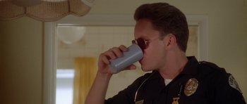 Movie still from “Short Cuts” (1993), directed by Robert Altman – A police officer drinking from a cup while wearing headphones; Close Up shot, Low angle