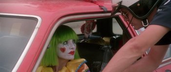 Movie still from “Short Cuts” (1993), directed by Robert Altman – A woman with a clown make - up sitting in the back seat of a pink car; Close Up shot, Over the shoulder angle