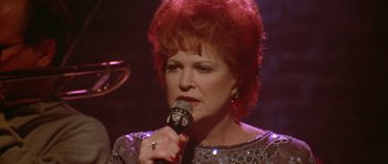 Movie still from “Short Cuts” (1993), directed by Robert Altman – An older woman is singing into a microphone; Close Up shot, High angle