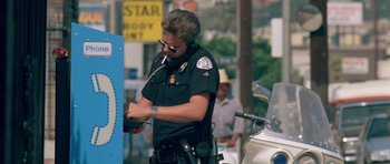 Movie still from “Short Cuts” (1993), directed by Robert Altman – A police officer standing next to a police car; Medium shot, Low angle