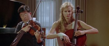 Movie still from “Short Cuts” (1993), directed by Robert Altman – A woman holding a cello while playing a violin in a room; Medium shot, Low angle