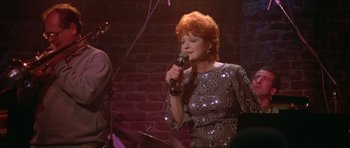 Movie still from “Short Cuts” (1993), directed by Robert Altman – A woman with red hair is singing into a microphone; Medium shot, High angle