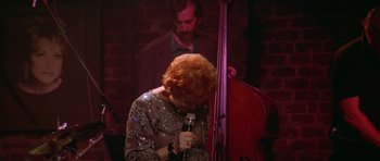 Movie still from “Short Cuts” (1993), directed by Robert Altman – A woman holding a microphone while standing in front of a double bass; Medium shot, High angle