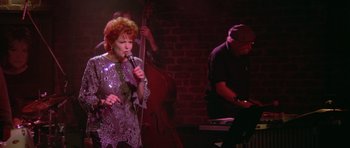 Movie still from “Short Cuts” (1993), directed by Robert Altman – A woman singing into a microphone in front of a band; Medium shot, High angle