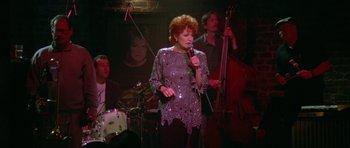 Movie still from “Short Cuts” (1993), directed by Robert Altman – A woman singing into a microphone in front of a group of people; Wide shot, High angle