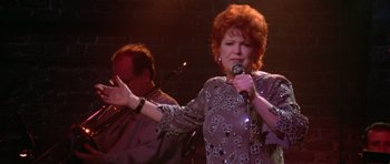 Movie still from “Short Cuts” (1993), directed by Robert Altman – An older woman singing into a microphone while a man watches; Medium shot, Low angle