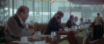 Movie still from “Short Cuts” (1993), directed by Robert Altman – A man sitting at a table in front of a window; Medium shot, Over the shoulder angle