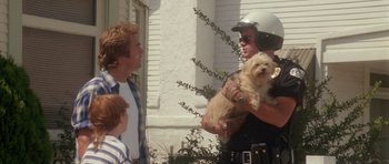 Movie still from “Short Cuts” (1993), directed by Robert Altman – A police officer holding a small dog while two other people look on; Medium shot, Low angle