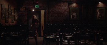 Movie still from “Short Cuts” (1993), directed by Robert Altman – A room filled with chairs and a woman standing in front of a door; Wide shot, High angle