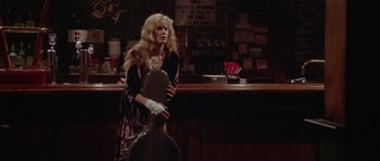 Movie still from “Short Cuts” (1993), directed by Robert Altman – A woman standing in front of a bar holding a guitar; Wide shot, Over the shoulder angle