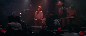 Movie still from “Short Cuts” (1993), directed by Robert Altman – A woman singing into a microphone on a stage; Wide shot, Over the shoulder angle