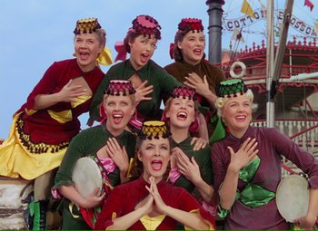 Movie still from “Show Boat” (1951), directed by George Sidney – A group of women in colorful outfits singing and dancing together; Medium shot, Low angle
