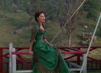 Movie still from “Show Boat” (1951), directed by George Sidney – A woman in a green dress sitting on top of a bridge; Wide shot, Low angle