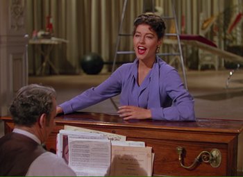 Movie still from “Show Boat” (1951), directed by George Sidney – A woman sitting at a desk in front of a man; Medium shot, High angle