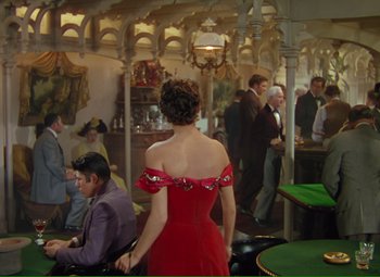 Movie still from “Show Boat” (1951), directed by George Sidney – A woman in a red dress standing next to a table; Wide shot, High angle