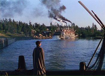 Movie still from “Show Boat” (1951), directed by George Sidney – A man standing on a dock looking at a boat; Extreme Wide shot, Over the shoulder angle