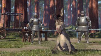 Movie still from “Shrek” (2001), directed by Vicky Jenson – A donkey sitting in the grass next to a bunch of people; Wide shot, Low angle
