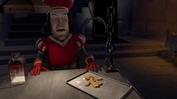 Movie still from “Shrek” (2001), directed by Vicky Jenson – A man sitting at a table next to a pan of cookies; Medium shot, High angle