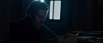 Movie still from “Siberia” (2020), directed by Abel Ferrara – A man sitting in a dark room looking at a book; Close Up shot, Low angle
