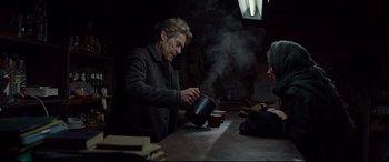 Movie still from “Siberia” (2020), directed by Abel Ferrara – An older woman pouring a cup of tea into a mug; Medium shot, Over the shoulder angle