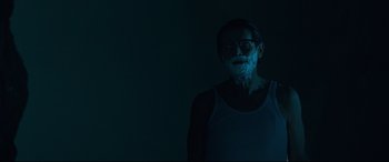 Movie still from “Siberia” (2020), directed by Abel Ferrara – A man in a white tank top is standing in the dark; Medium shot, Low angle