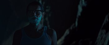 Movie still from “Siberia” (2020), directed by Abel Ferrara – A man with a beard and glasses is standing in the dark; Close Up shot, Over the shoulder angle