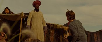 Movie still from “Siberia” (2020), directed by Abel Ferrara – A man wearing a turban talking to another man in front of a building; Medium shot, Over the shoulder angle