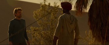 Movie still from “Siberia” (2020), directed by Abel Ferrara – A man wearing a red turban walks in front of a tree; Wide shot, Over the shoulder angle