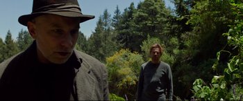 Movie still from “Siberia” (2020), directed by Abel Ferrara – Two men standing next to each other near a forest; Medium shot, Over the shoulder angle