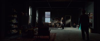 Movie still from “Siberia” (2020), directed by Abel Ferrara – A person sitting in a dark room in a dark room; Wide shot, High angle