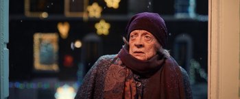 Movie still from “A Boy Called Christmas” (2021), directed by Gil Kenan – An older woman wearing a purple hat and a purple scarf; Close Up shot, Over the shoulder angle