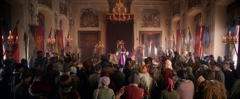 Movie still from “A Boy Called Christmas” (2021), directed by Gil Kenan – A crowd of people sitting in a large room; Wide shot, Over the shoulder angle
