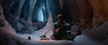 Movie still from “A Boy Called Christmas” (2021), directed by Gil Kenan – A man sitting on the ground next to a branch; Wide shot, High angle
