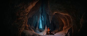 Movie still from “A Boy Called Christmas” (2021), directed by Gil Kenan – A person sitting in a cave with a light shining through; Extreme Wide shot, High angle
