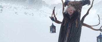 Movie still from “A Boy Called Christmas” (2021), directed by Gil Kenan – A man in a fur coat and a bird cage hanging from a tree branch; Medium shot, Low angle