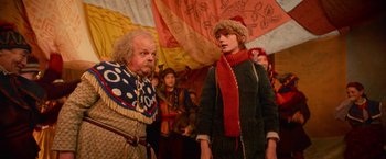 Movie still from “A Boy Called Christmas” (2021), directed by Gil Kenan – A man and a woman standing next to each other in front of a crowd; Medium shot, Over the shoulder angle