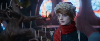 Movie still from “A Boy Called Christmas” (2021), directed by Gil Kenan – A young girl wearing a hat and a scarf in front of a stained glass window; Close Up shot, Low angle