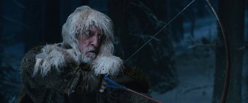 Movie still from “A Boy Called Christmas” (2021), directed by Gil Kenan – A man with a beard and a fur hat holding a bow and arrow; Medium shot, Low angle